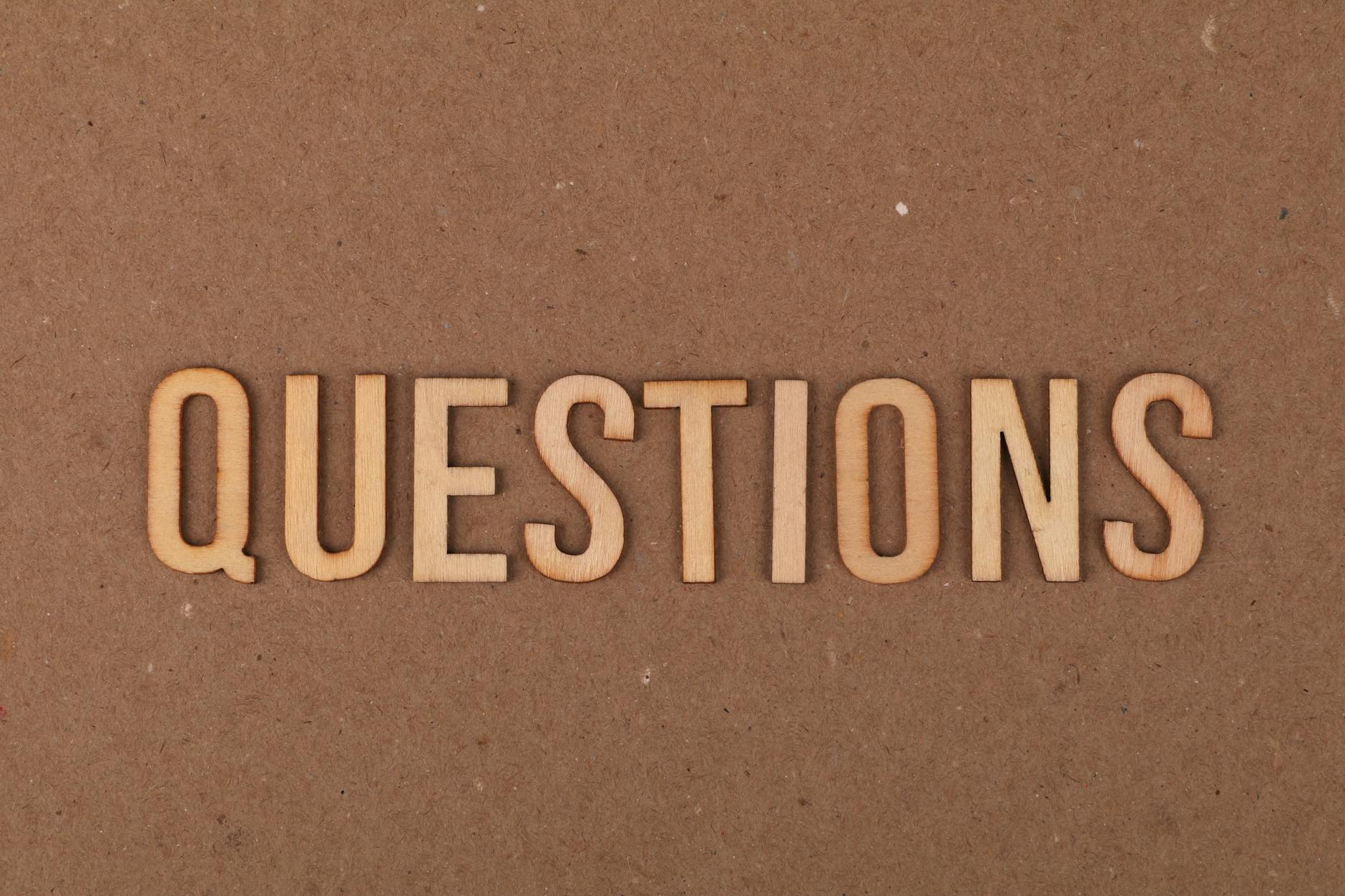 Wooden letters spelling the word 'QUESTIONS' on a cardboard background, providing a neutral copyspace.
