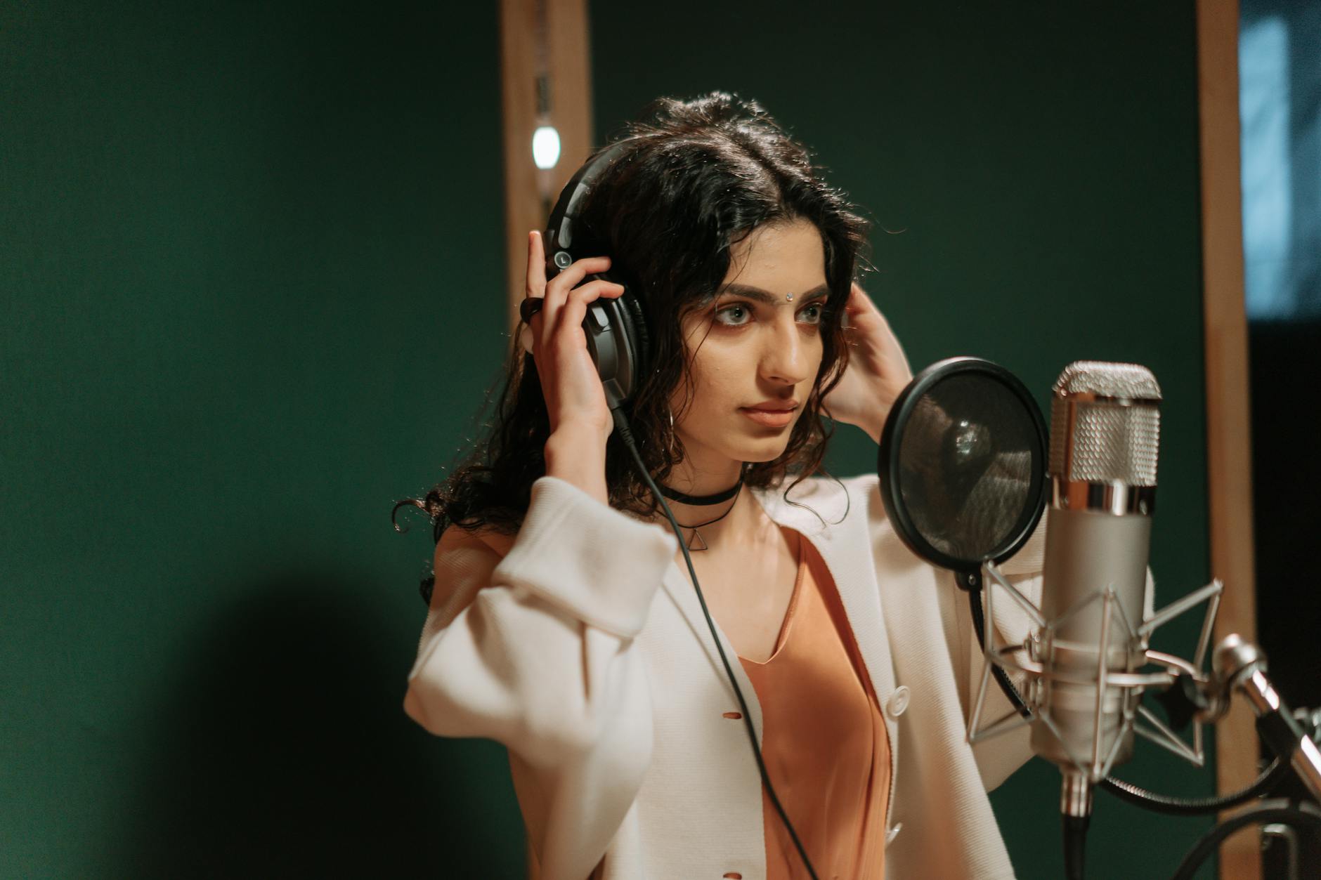 A woman wearing headphones recording vocals in a music studio with a microphone.