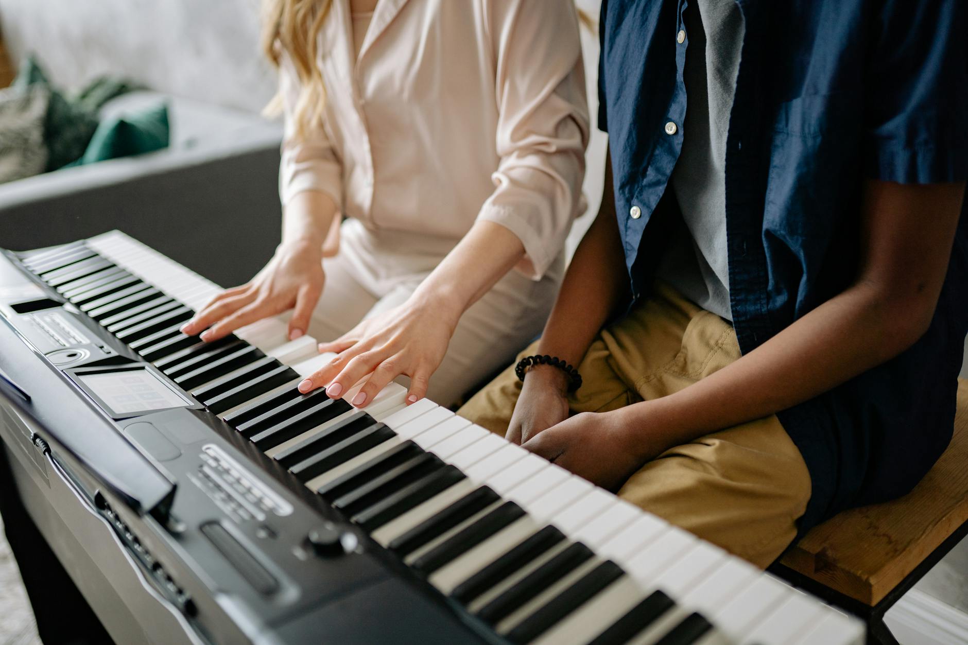 Two people playing an electronic keyboard together, showcasing musical collaboration.