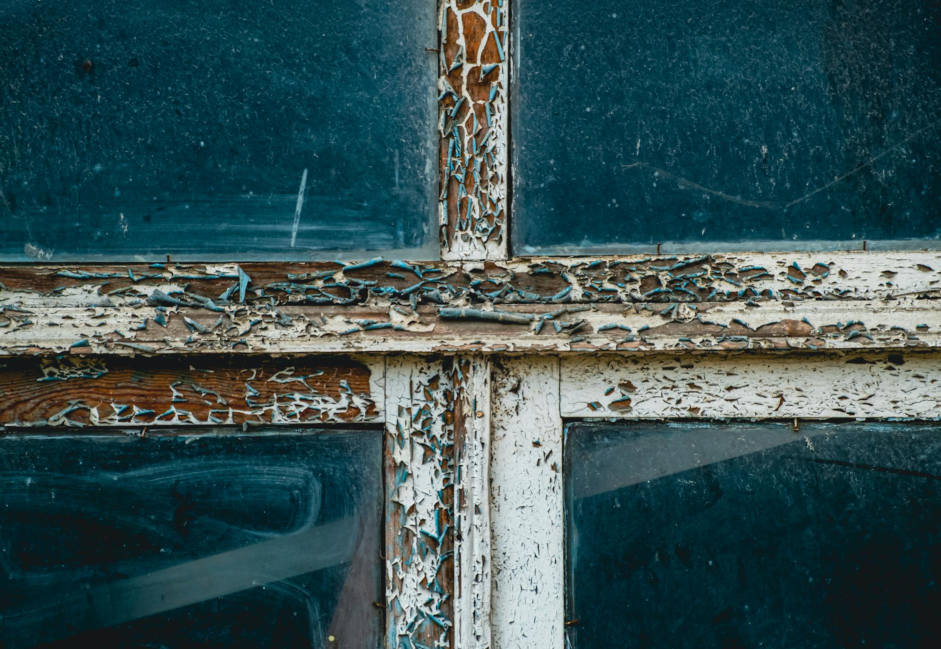 Detailed view of peeling paint on a rustic wooden window frame, showcasing texture and decay.