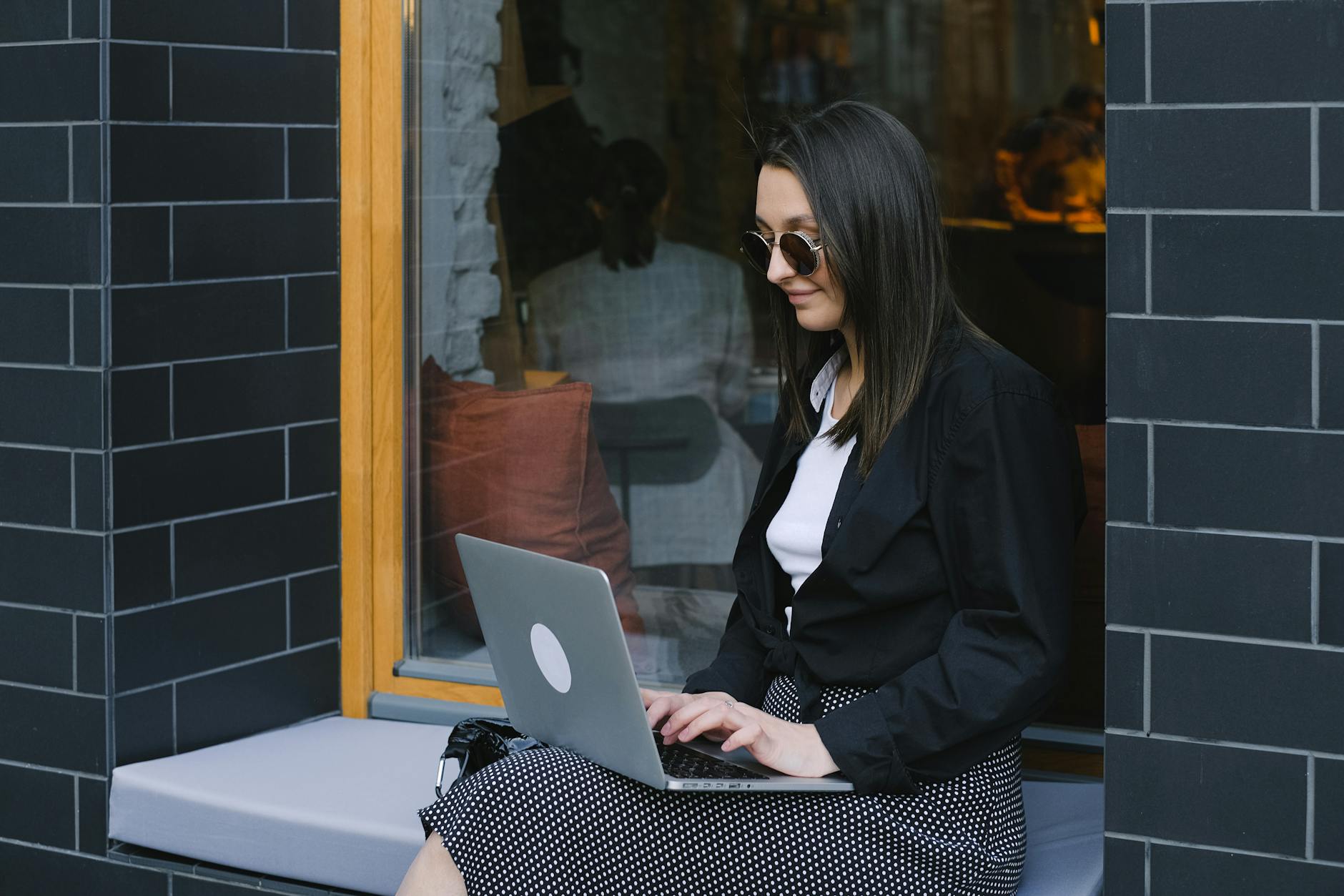 Jak zmienić skróty klawiaturowe w Windows 11 — PowerToys, AutoHotkey i inne metody krok po kroku 4 Young woman using laptop by a window in an urban environment, enjoying remote work outdoors.