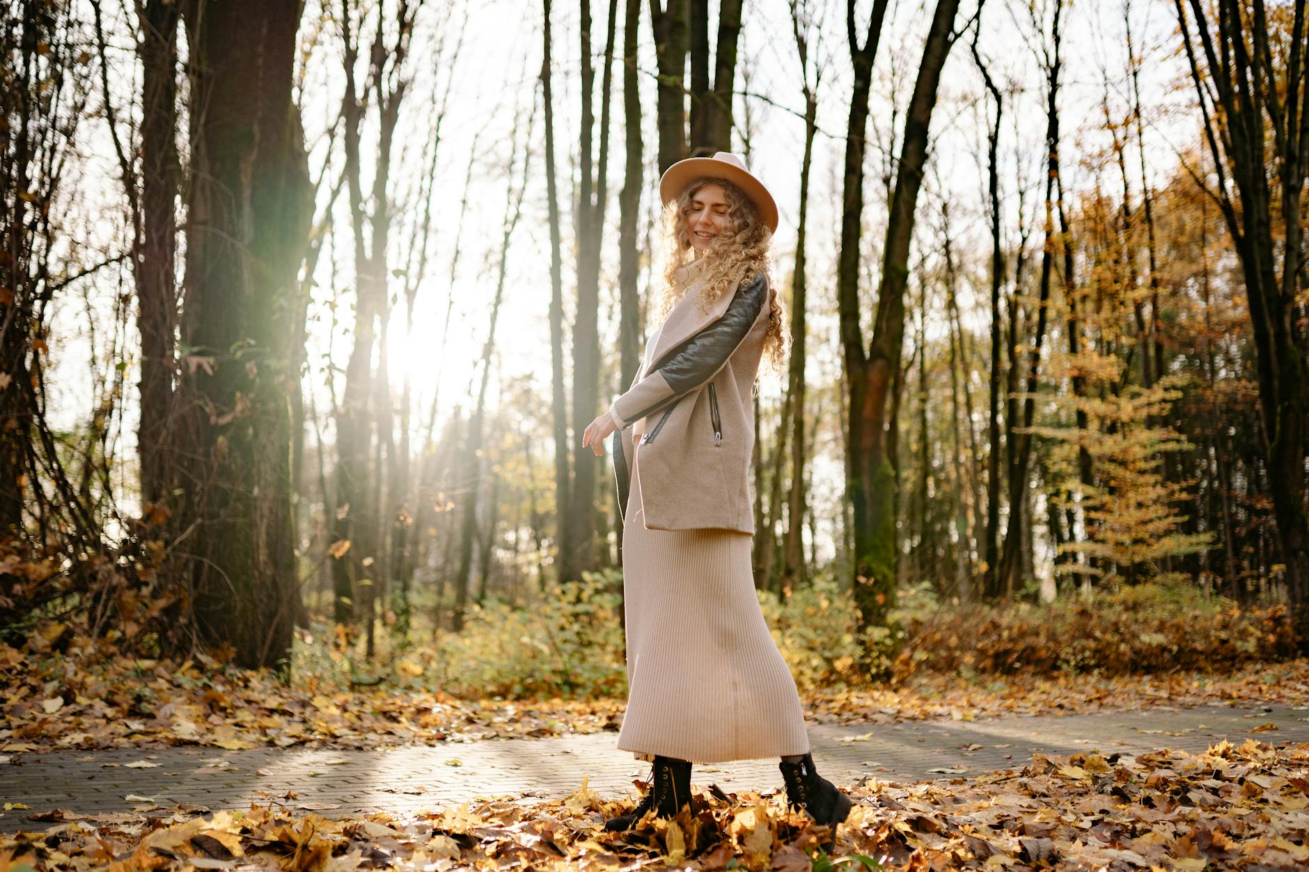 Woman enjoying a sunny autumn day walking through a forest of fallen leaves.