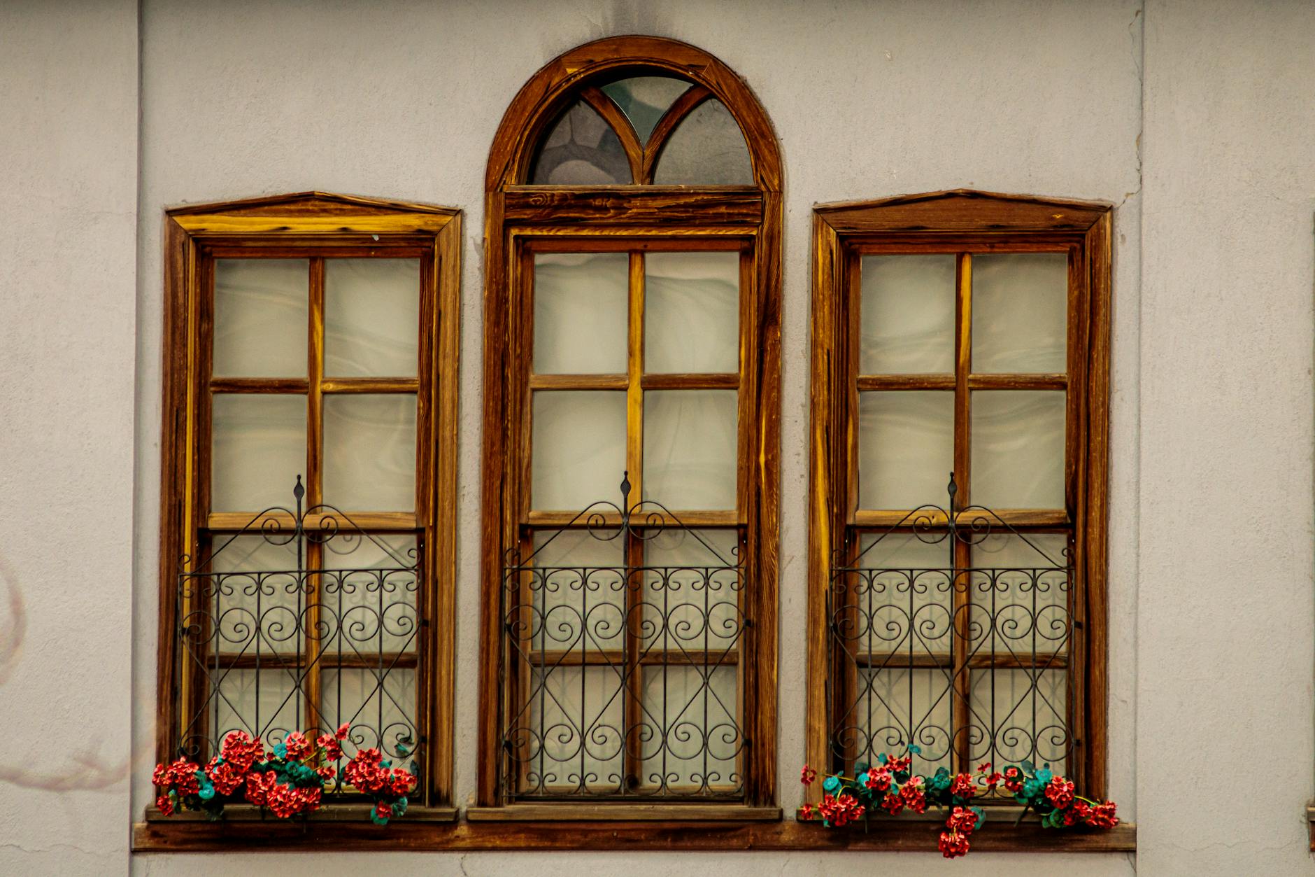 Three wooden windows with vibrant flower boxes on a vintage facade.