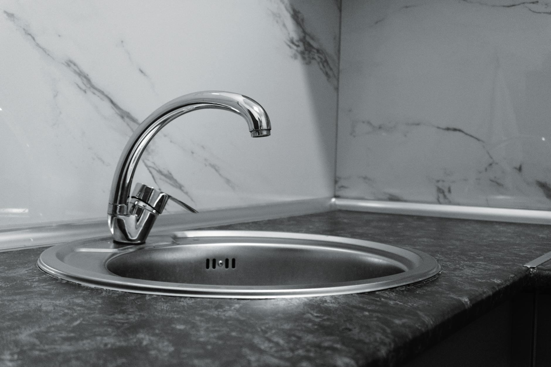 Stainless steel kitchen sink and faucet against marble backsplash in a modern kitchen.