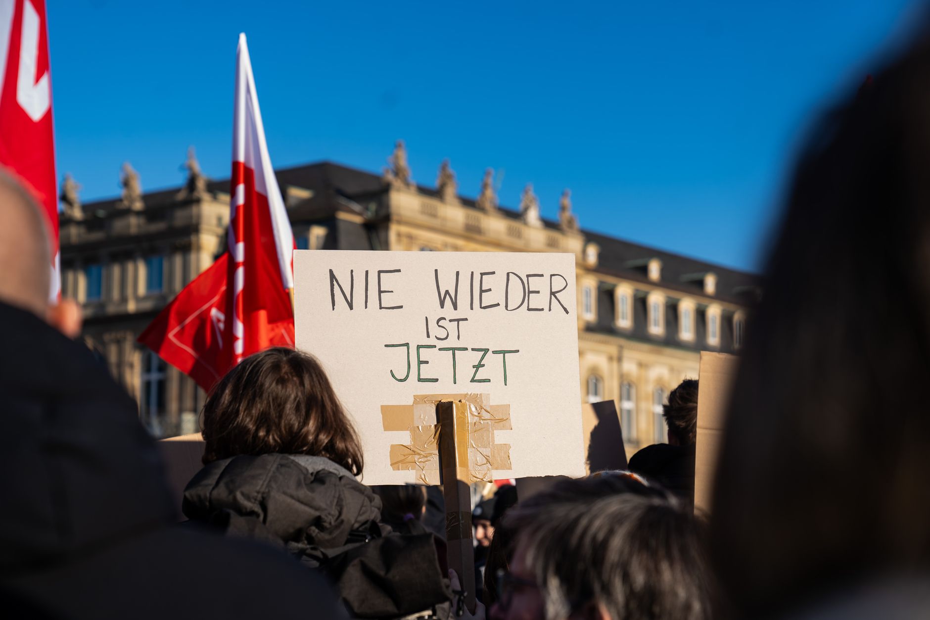 Demonstration in Stuttgart, Germany with protest signs and flags under a clear blue sky.